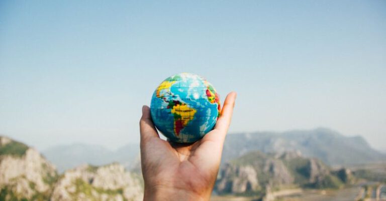 Travel - Person Holding World Globe Facing Mountain